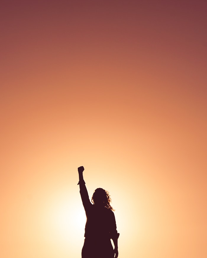 A woman in silhouette holds her fist up in the air.